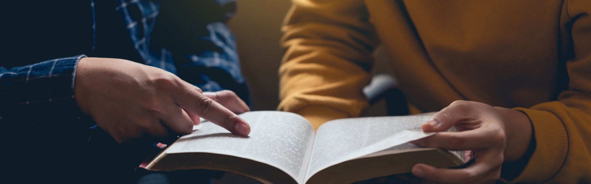 Male reading the Holy Bible by pointing to the character and sharing the gospel with a friend.