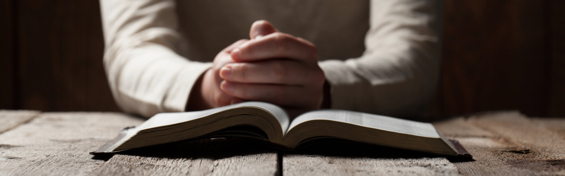Woman hands praying with a bible in a dark over wooden table